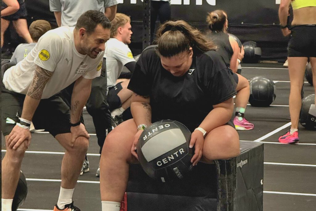 Deelnemer aan de adaptive HYROX-race met begeleiding van een coach