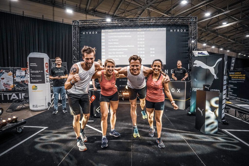 Een relayteam van vier komt samen over de finish van een HYROX-race