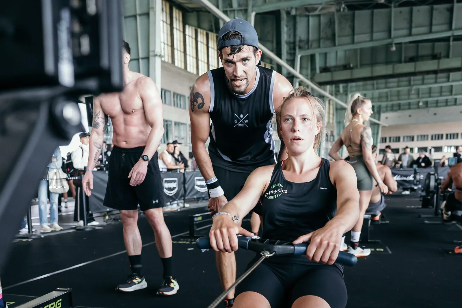 Arnoud Dorlijn coacht een atleet in D-Physics-tenue op de roeiergometer tijdens HYROX